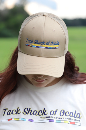 Person wearing a beige cap and white shirt with 'Tack Shack of Ocala' branding outdoors.