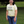 Person wearing a light yellow t-shirt with text standing in a grassy area.