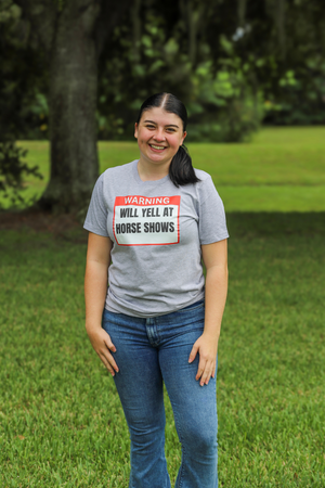 Person wearing a gray t-shirt with a humorous warning label in an outdoor setting