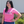 Woman wearing a pink t-shirt with text, standing outdoors against a white wall.