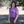 Woman wearing a purple shirt and gray pants standing outdoors with trees in the background